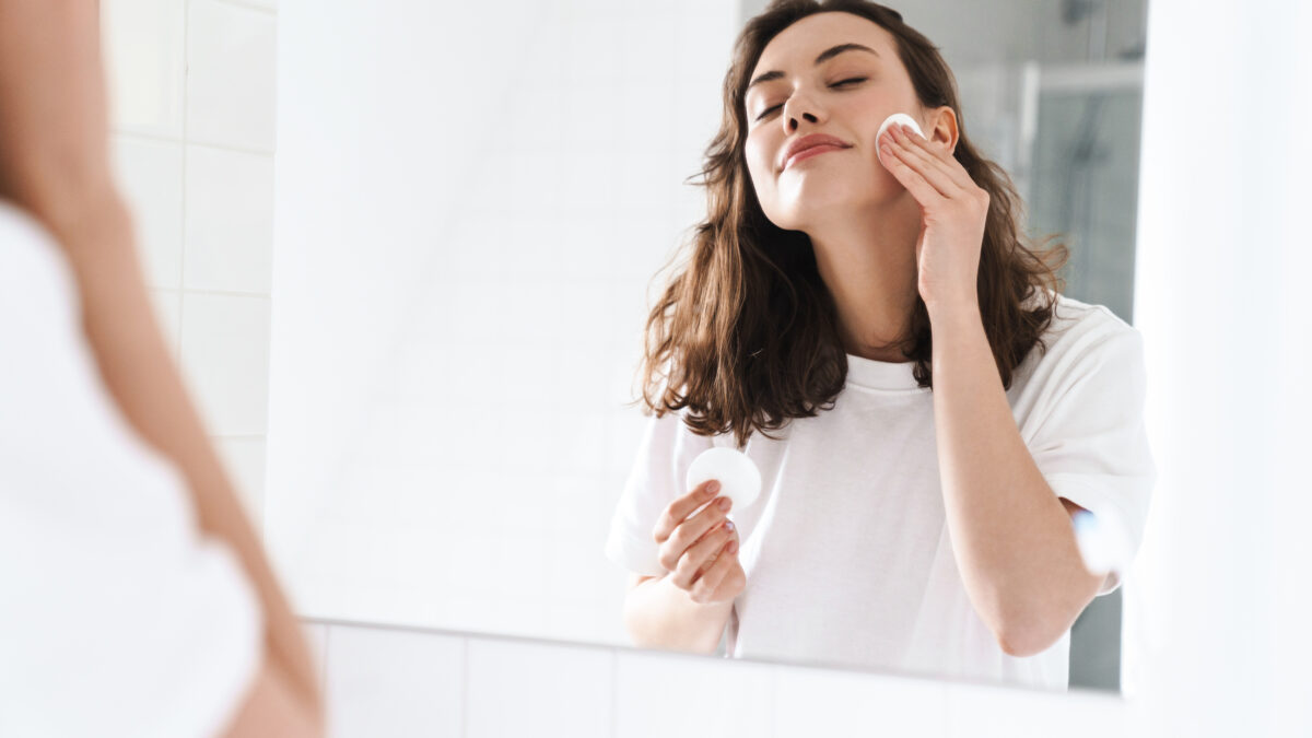 Photo Of Woman Cleaning Her Face With Cotton Pad While Looking At Mirror